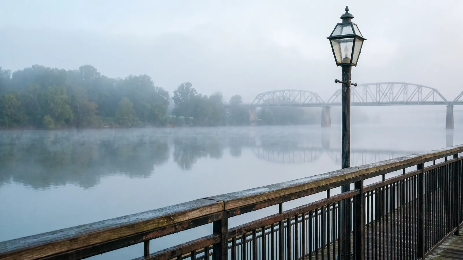 The Cumberland River at Clarksville, Tennessee on a misty morning, the riverwalk railing in the foreground and a bridge spanning the water in the distance